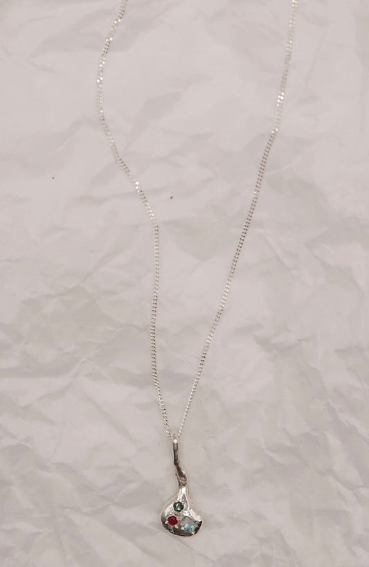 Silver necklace with a pendant embedded with colurful stones on a textured gray surface