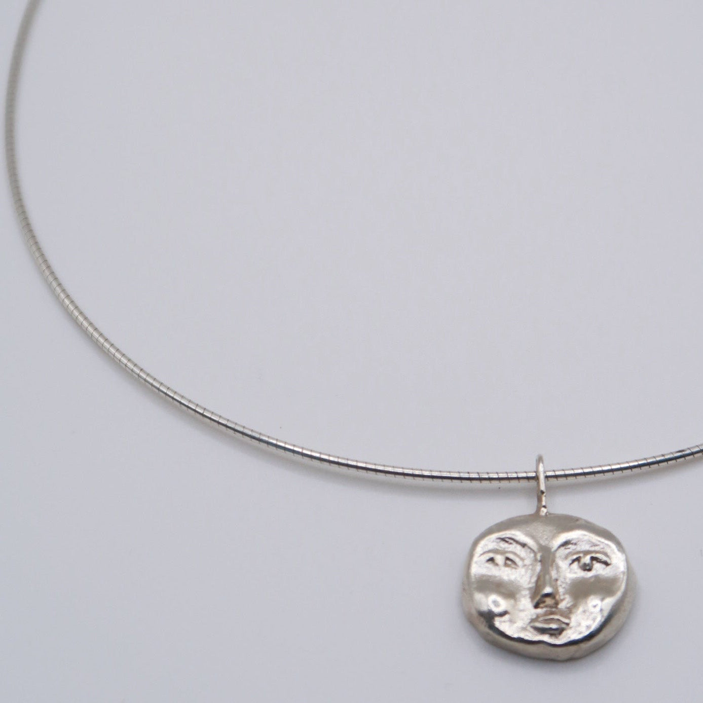 Silver necklace with a face pendant on a light gray background