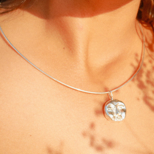 Close-up of a necklace with a pendant on a person's neck, with a blurred background.