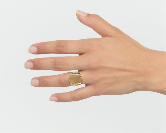 Hand wearing a gold ring on a plain background