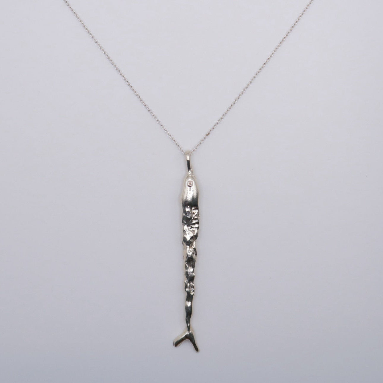 Silver necklace with a fish pendant in silver  on a light gray background