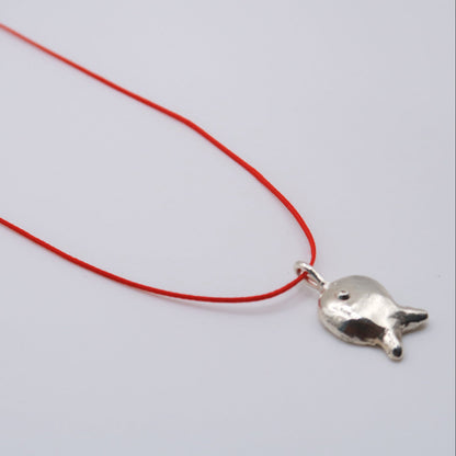 Silver fish pendant on a red string against a white background