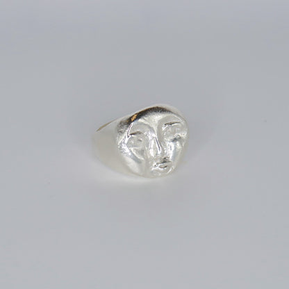 Silver ring with a face design on a light gray background