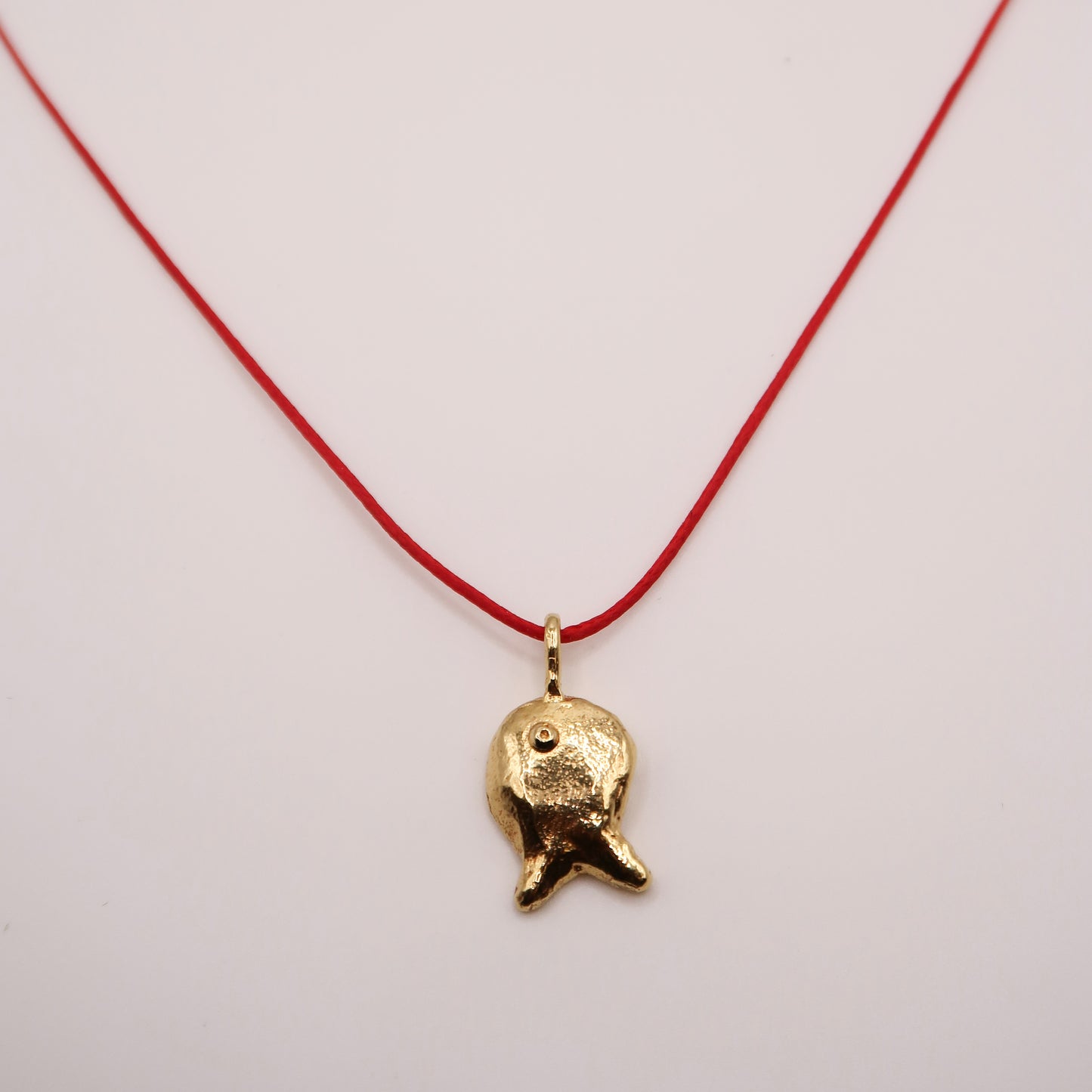 Gold fish pendant on a red string against a light background
