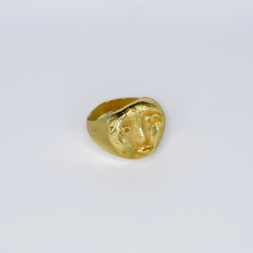 Gold ring with face design on a light gray background