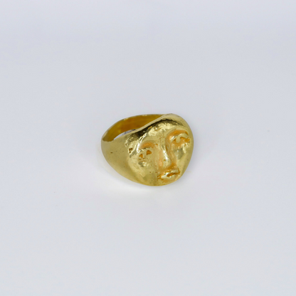 Gold ring with face design on a light gray background