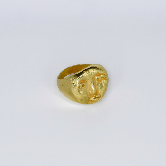 Gold ring with face design on a light gray background