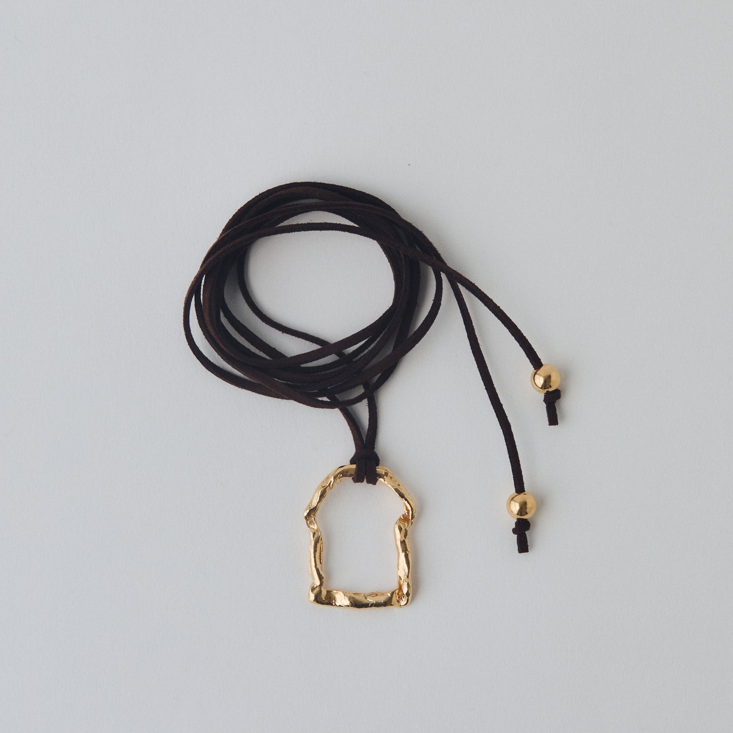Brown cord necklace with a gold pendant on a light gray background