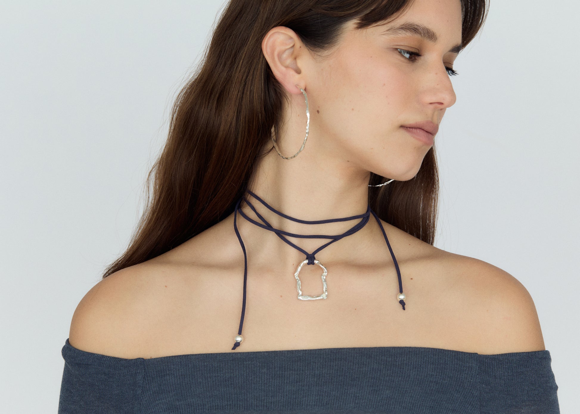 Woman wearing a layered neck choker and hoop earrings on a plain background