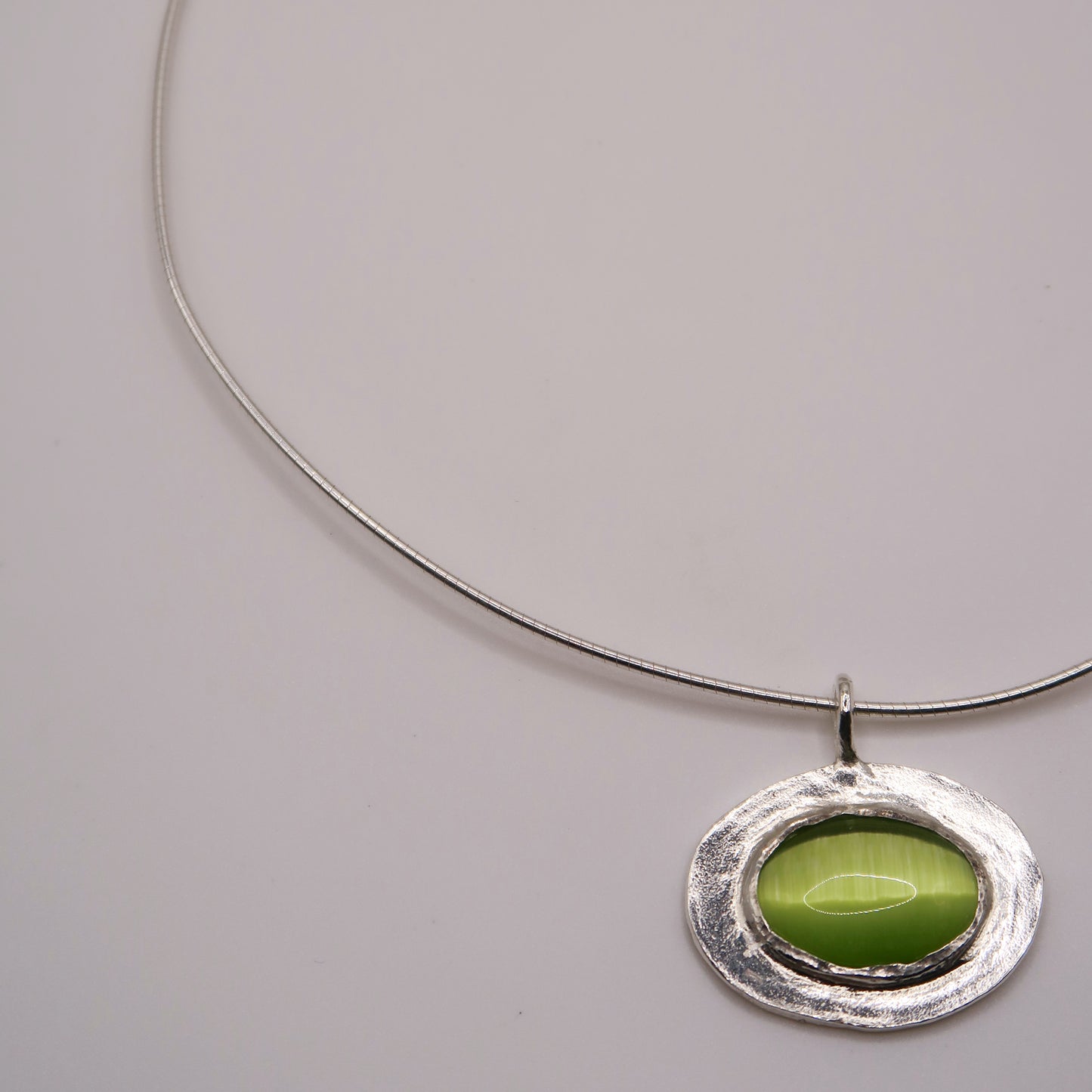 Silver necklace with a green pendant on a light gray background