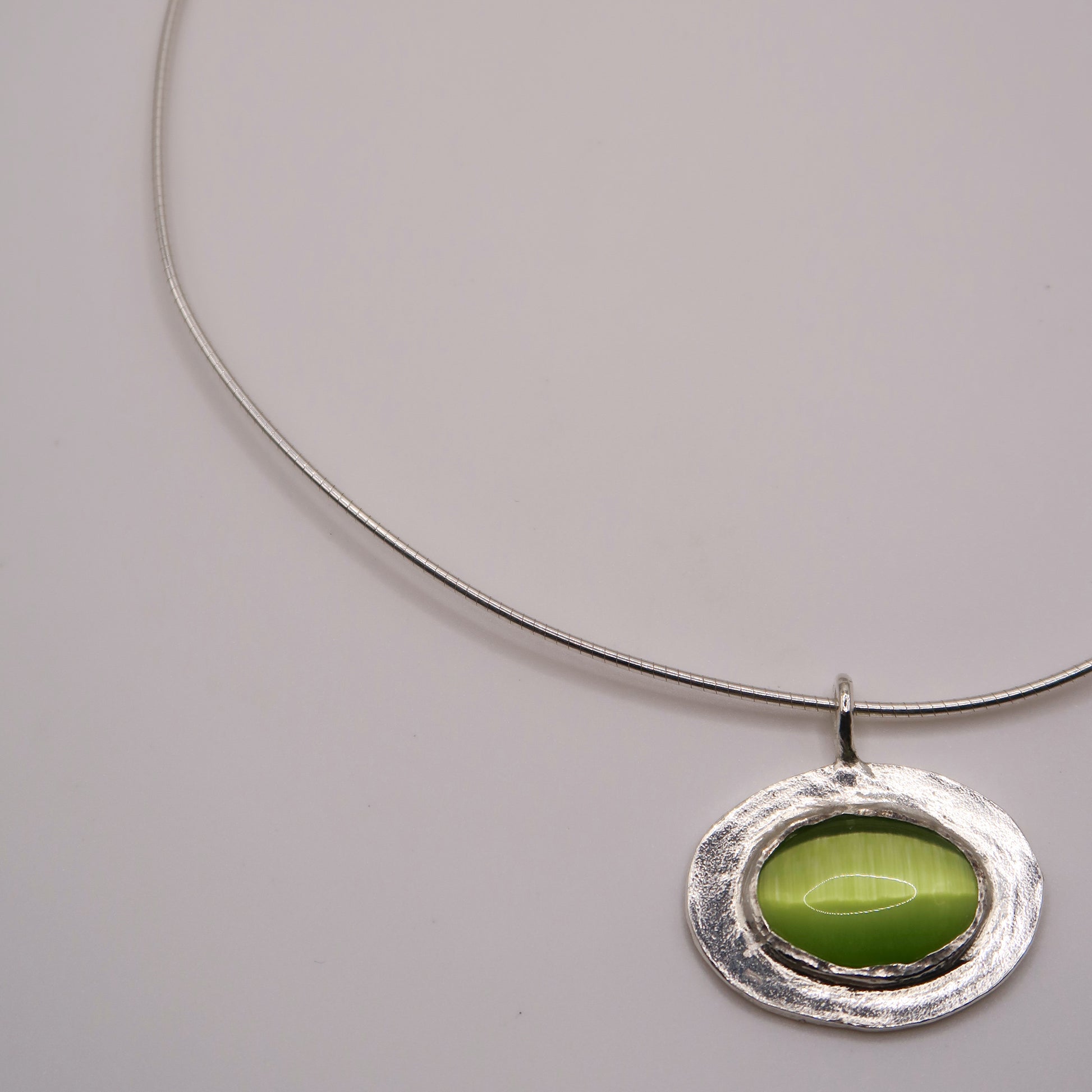 Silver necklace with a green pendant on a light gray background