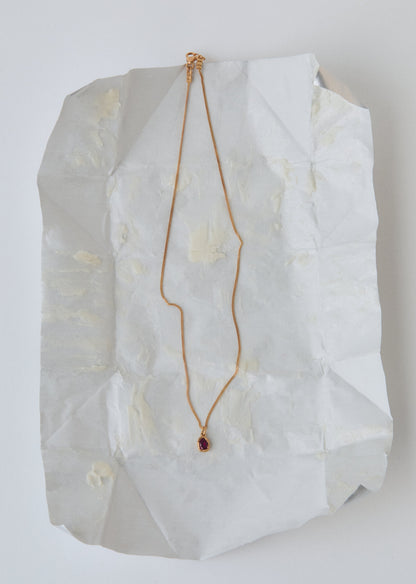 Gold necklace with a red gemstone on a white textured surface