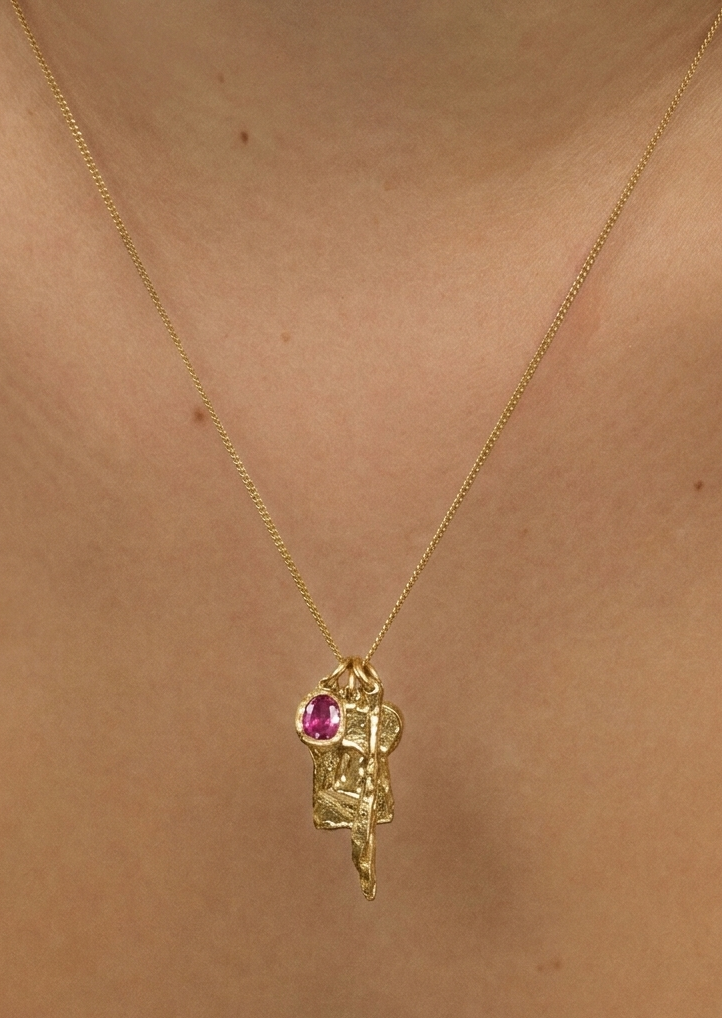 Gold necklace with a pink gemstone pendant on a person's neck