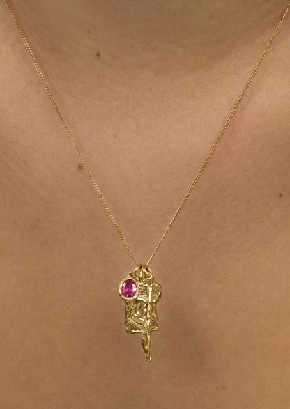 Gold necklace with a pink gemstone pendant on a person's neck
